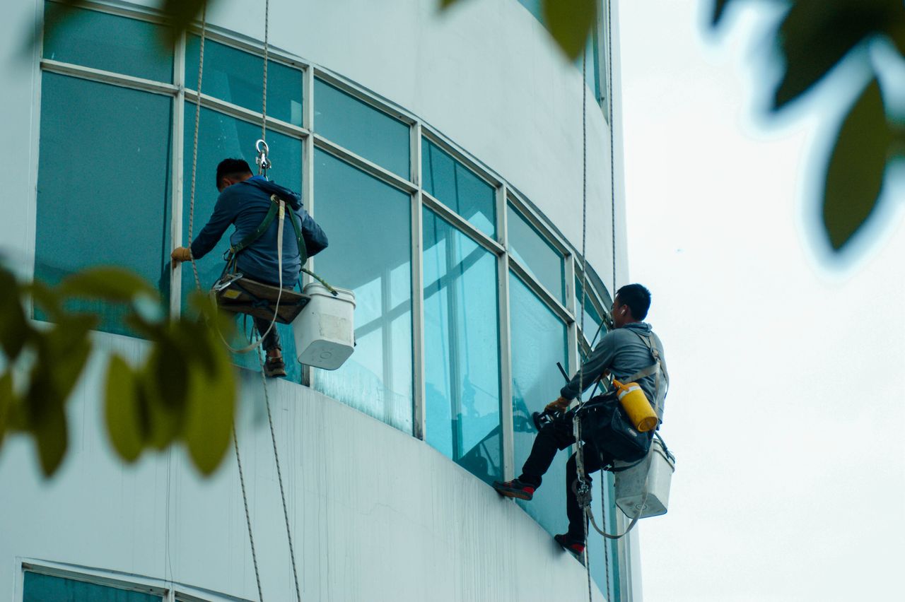 why-choose-us Window cleaners suspended on ropes clean a high-rise buildings glass exterior.